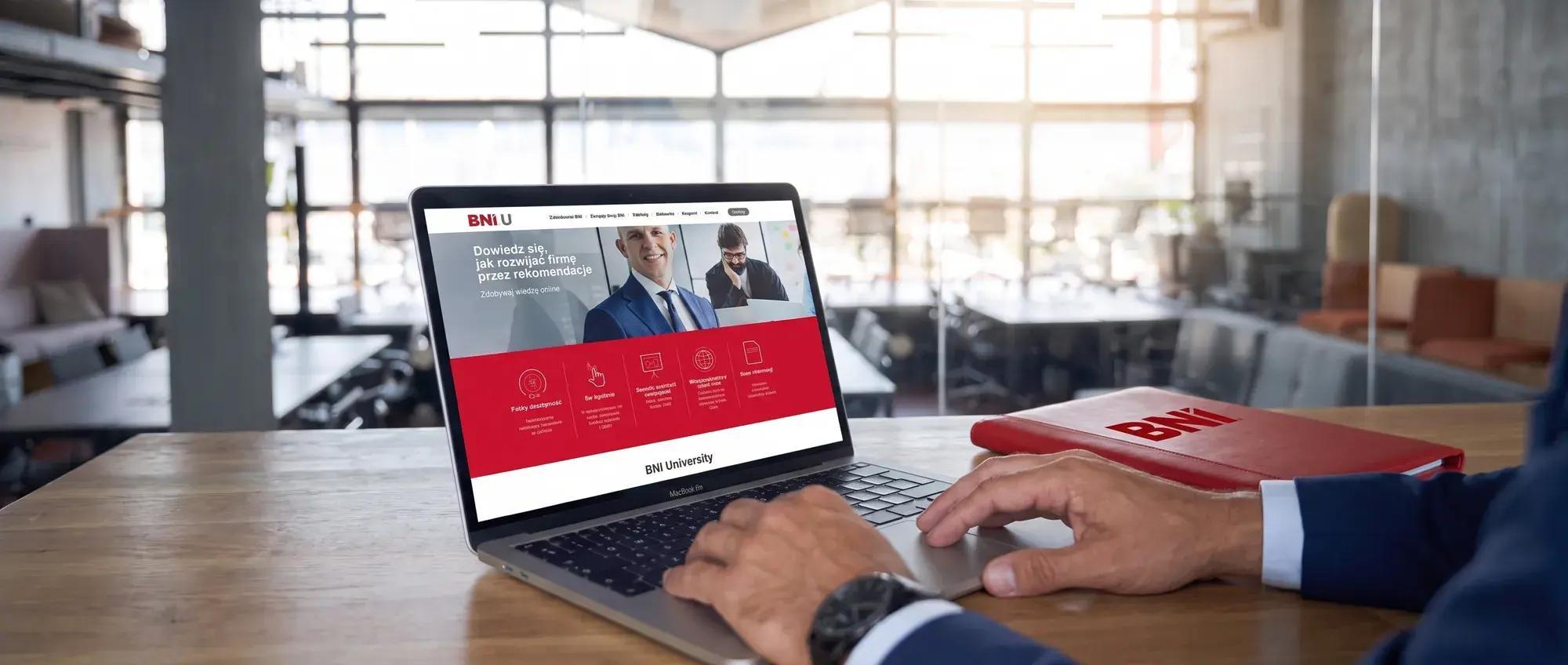 Dłonie na laptopie z platformą BNI University, obok czerwona teczka