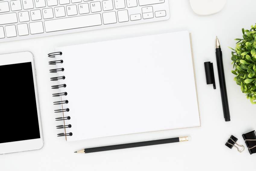 White office desk table with blank notebook page and supplies. Top view with copy space, flat lay.